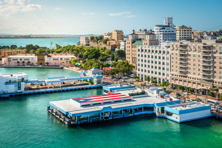 Colorful image of the cruise and ferry harbor of San Juan in Puerto Rico. Puerto Rican flag on platform above the water pier. Tall buildings at the cruise port terminal.