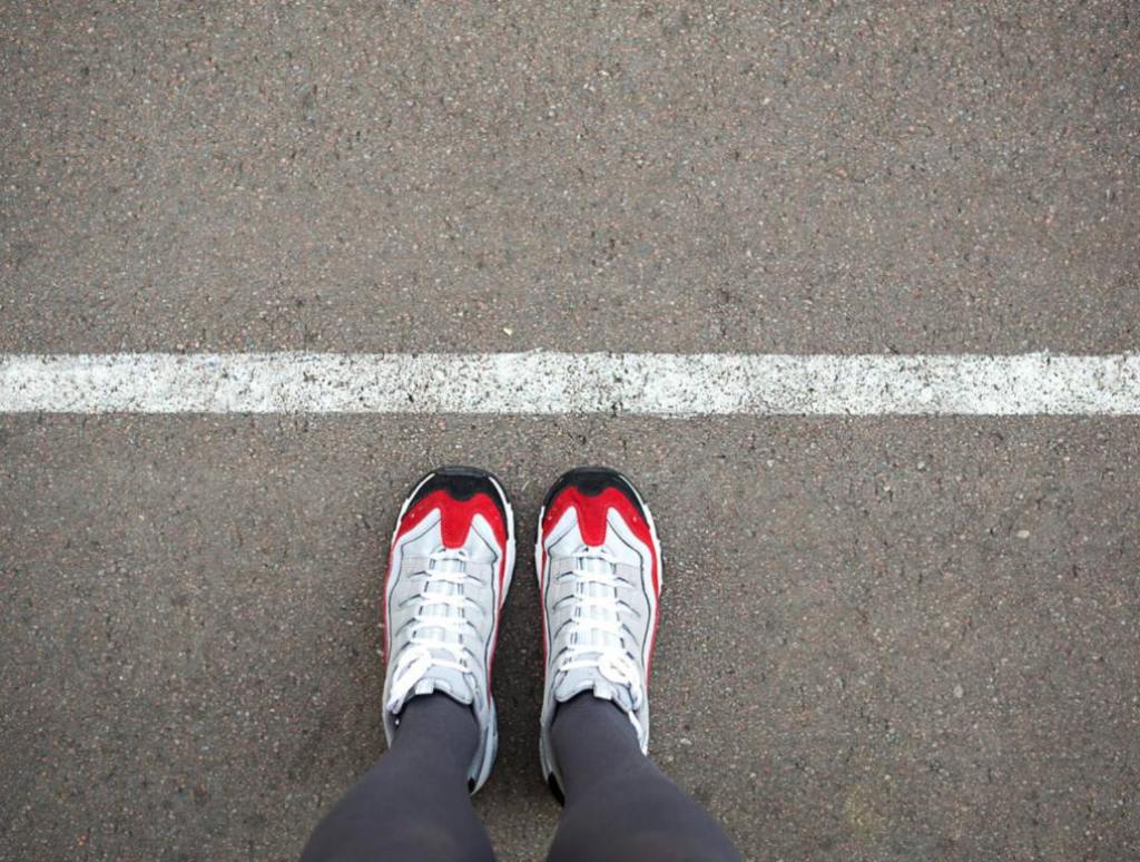 Feet in sneakers stand near the dividing line on the asphalt. Bounding line, social distance, waiting in line. The border, stand in line for a start.